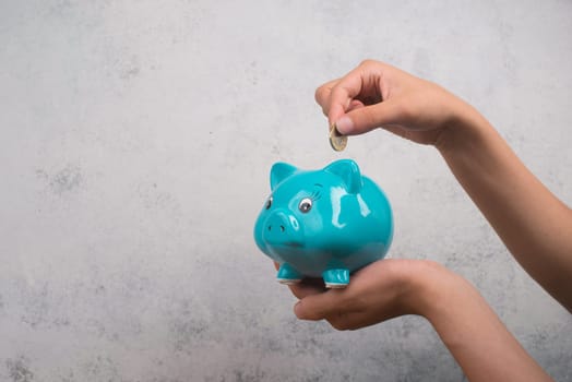 Putting money into a blue piggy bank, empty copy space for text