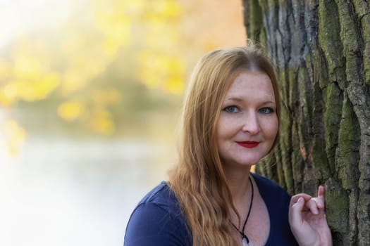 Portrait of freckled young woman  with red lips is posing in autumn park. The woman is looking at the camera.