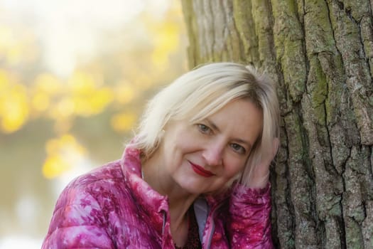 Portrait of middle aged woman in autumn park. The woman is looking at the camera.