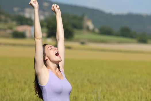 Excited woman raising arms and screaming celebrating summer vacation in a wheat field