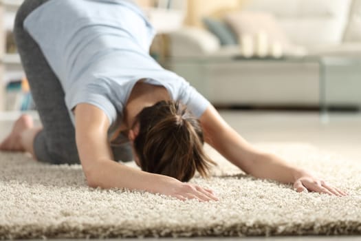 Female exercising yoga melting heart pose on a carpet in the living room at home