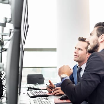 Successful businessmen trading stocks. Stock traders looking at graphs, indexes and numbers on multiple computer screens. Colleagues in traders office. Business success.