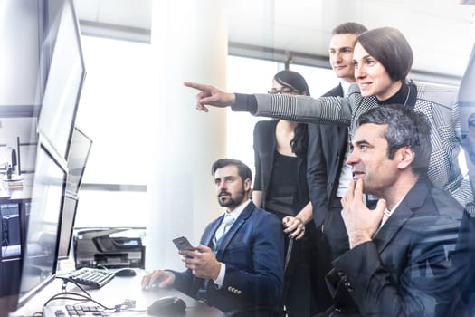Business people looking at data on multiple computer screens in corporate office. Businesswoman pointing on screen. Business team trading online. Business, entrepreneurship and team work concept.
