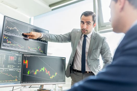 Businessmen trading stocks online. Stock brokers looking at graphs, indexes and numbers on multiple computer screens. Colleagues in discussion in traders office. Business success concept.
