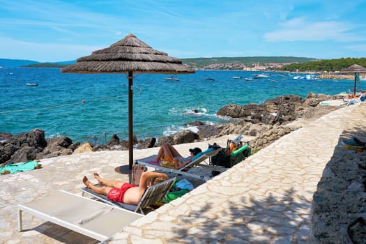 Holidaymakers sunbathing at a typical bathing spot on the rocky coast near Krk in Croatia
