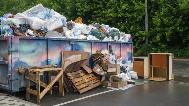 Metal durable blue industrial trash bin for outdoor trash at construction site. Large waste basket for household or industrial waste. A pile of waste. Ukraine, Kiev - August 09, 2021
