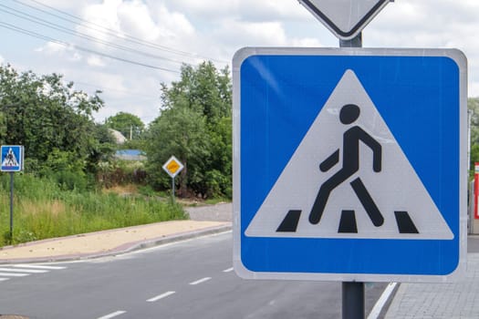 Pedestrian overground crossing, old square white with blue reflective road sign, outdoors close-up. Zebra and human sign on the background of the city. Pedestrian crossing sign