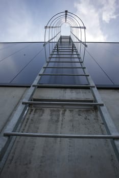 Fire escape on the industrial building above, bottom view. Stainless steel handrails, roof ladder. Detail view of stairs with safety cage. Building construction concept