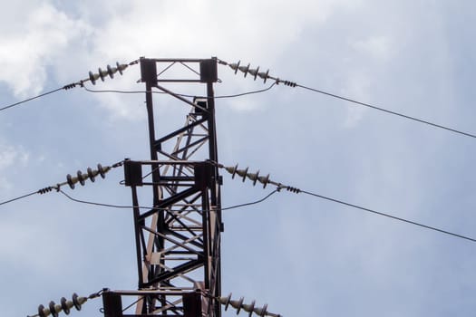 High voltage electrical tower. Power lines and power pylons on a sunny day with circular clouds in the blue sky. High voltage power transmission line supports. They have a complex steel structure