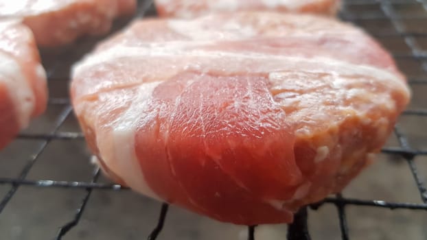 Raw meat cutlets wrapped in bacon are cooked on the grill rack. The chef prepares the grilled burger patties. Ingredients for making a hamburger. Meat lovers concept. Fast food