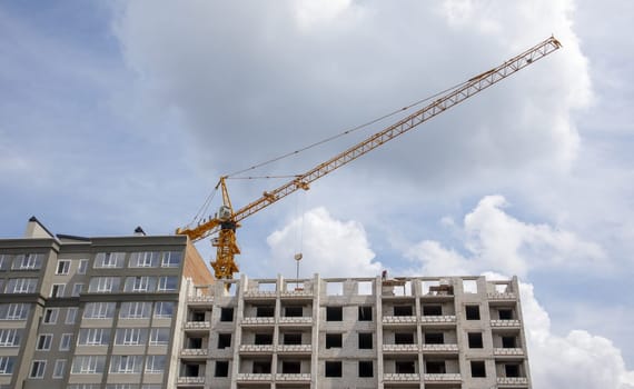 Construction crane on an unfinished residential building against the sun and blue sky. Housing construction, apartment building in the city. Construction site of residential buildings