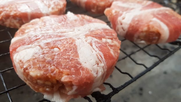 Raw meat cutlets wrapped in bacon are cooked on the grill rack. The chef prepares the grilled burger patties. Ingredients for making a hamburger. Meat lovers concept. Fast food
