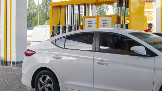 The white car is refueling. Refueling a car that is parked at a gas station. Refuel cars with a gasoline pump. Oil and gas energy. Ukraine, Kiev -15 August, 2021