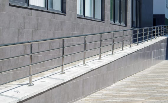 A ramp with stainless steel handrails for wheelchairs, bicycles and strollers with children in front of the building. Handrail for lifting a wheelchair. Shiny stainless steel handrail