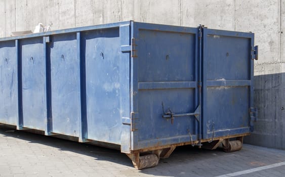 Metal durable blue industrial trash bin for outdoor trash at construction site. Large waste basket for household or industrial waste. A pile of waste