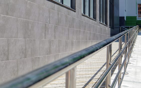 A ramp with stainless steel handrails for wheelchairs, bicycles and strollers with children in front of the building. Handrail for lifting a wheelchair. Shiny stainless steel handrail
