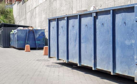 Metal durable blue industrial trash bin for outdoor trash at construction site. Large waste basket for household or industrial waste. A pile of waste
