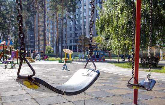 Close up empty baby swing in the park. New chain swing. Set of black swing chains on a modern playground. Focus on the swing in the blurry background