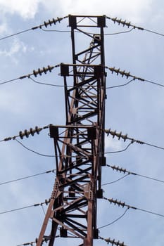 High voltage electrical tower. Power lines and power pylons on a sunny day with circular clouds in the blue sky. High voltage power transmission line supports. They have a complex steel structure