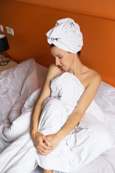 Young girl with clean skin with a towel on her head lying in bed, resting after a shower, relaxing at home