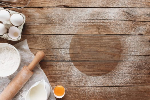 Baking ingredients, kitchen utensils on old wooden background. Cooking dough, preparing egg yolk, flour, rolling pin, milk, parchment paper, whisk, salt, sodium. Concept flat lay photo with copy space