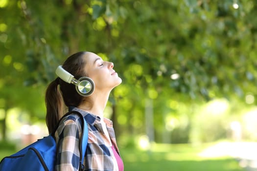 Side view portrait of a student wearing wireless headphones breathing fresh air in a campus