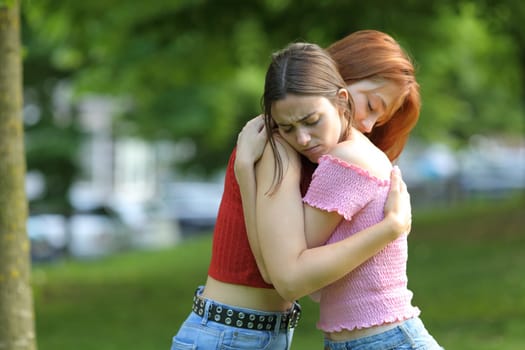 Sad women reconciling hugging in a green park