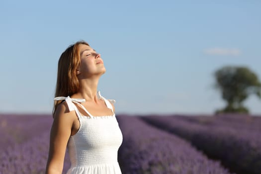 Happy woman wearing white dress breathing fresh air in lavender field