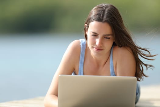 Front view portrait of a woman checking laptop content in a lake pier