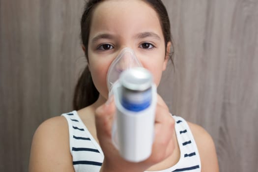Child girl using medical spray for breath. Inhaler, spacer and mask. Front view