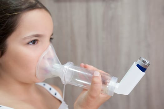 Child girl using medical spray for breath. Inhaler, spacer and mask. Side view