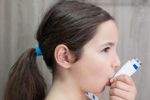 Child girl using medical spray for breath. Inhaler. Side view