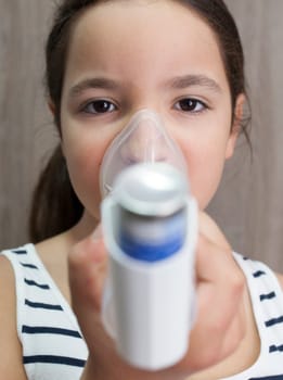 Child girl using medical spray for breath. Inhaler, spacer and mask. Front view