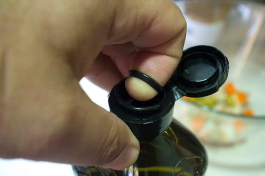 Finger opening a sealed olive oil bottle with an inner pull-off plastic tab underneath the cap. Closeup