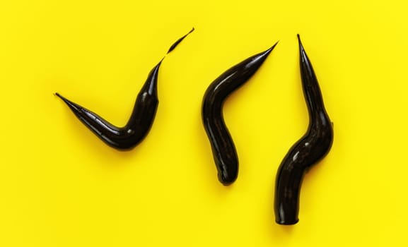 Three thick black cream smears charcoal toothpaste on yellow background, view from above.
