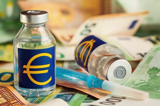 Vaccine price, cost or capital injection concept - glass vial and eur sign on pile of euro bank notes, syringe near, closeup detail.
