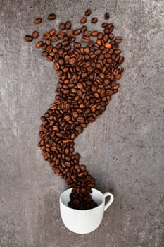 Spilled cup of coffee with roasted  beans forming a smoke shape, vertical