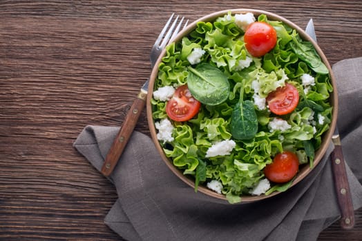 Healthy Green salad with fresh tomato and fresh cheese on wooden background close up