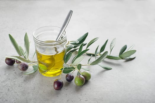 Glass of olive oil and Branch with olives and leaves background close up. Healthy olive oil concept