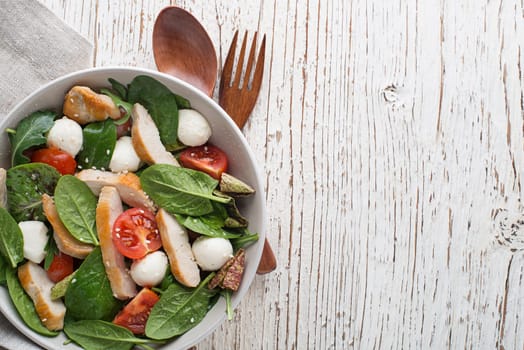 Healthy green salad with chicken breast, tomato and cheese on wooden table