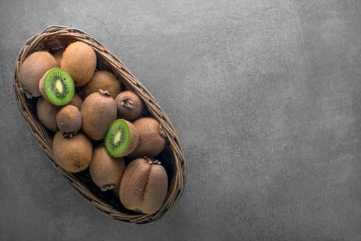 Ripe whole kiwi fruit and half kiwi fruit in basket on grey table background