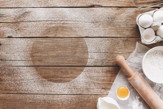 Baking ingredients, kitchen utensils on old wooden background. Cooking dough, preparing egg yolk, flour, rolling pin, milk, parchment paper, whisk, salt, sodium. Concept flat lay photo with copy space