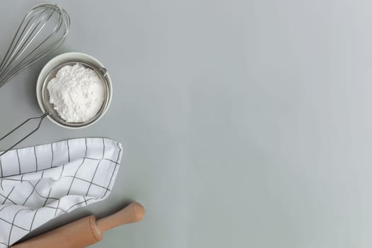 Baking ingredients, kitchen utensils, cooking concept on grey background flat lay, copy space. Prepare dough, bowl flour, rolling pin, whisk, kitchen towel, salt, soda, sieve. Photo on kitchen table