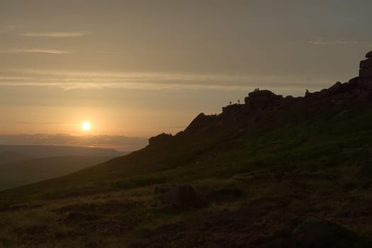 Climbers, couples and tourists line the rocky ridge of stanage edge at sunset. Many people enjoying the outdoors, wide angle perspective.