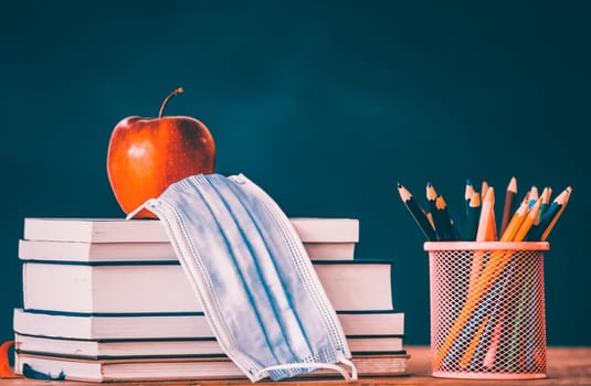 Back to school after coronavirus pandemic. School stationery supplies, medical masks over blackboard background.Concept of learning, maintaining social distance.