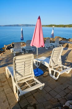 Parasols and sun loungers at a typical bathing place on the coast of the town of Krk on the Adriatic Sea in Croatia