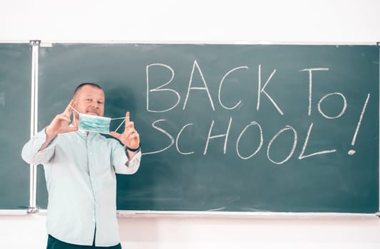 Teacher with face mask welcoming children back at school after lockdown. Back to school during COVID-19 pandemic.