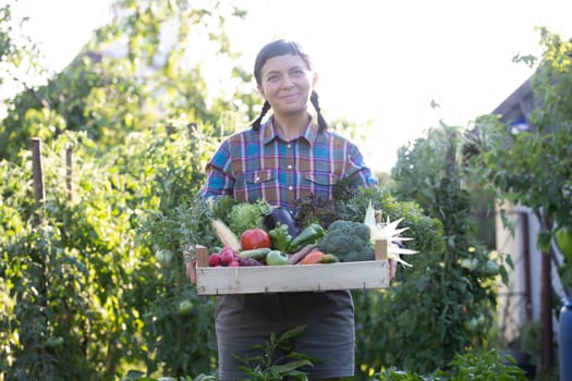 Farmer woman holding wooden box full of fresh raw vegetables. Growing organic food concept