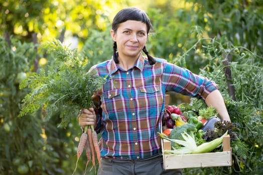 Farmer woman holding wooden box full of fresh raw vegetables. Growing organic food concept