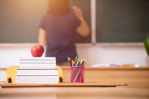 Back to School Concept. Apple, accessories and books in the classroom, chalkboard and teacher teaching in the background.